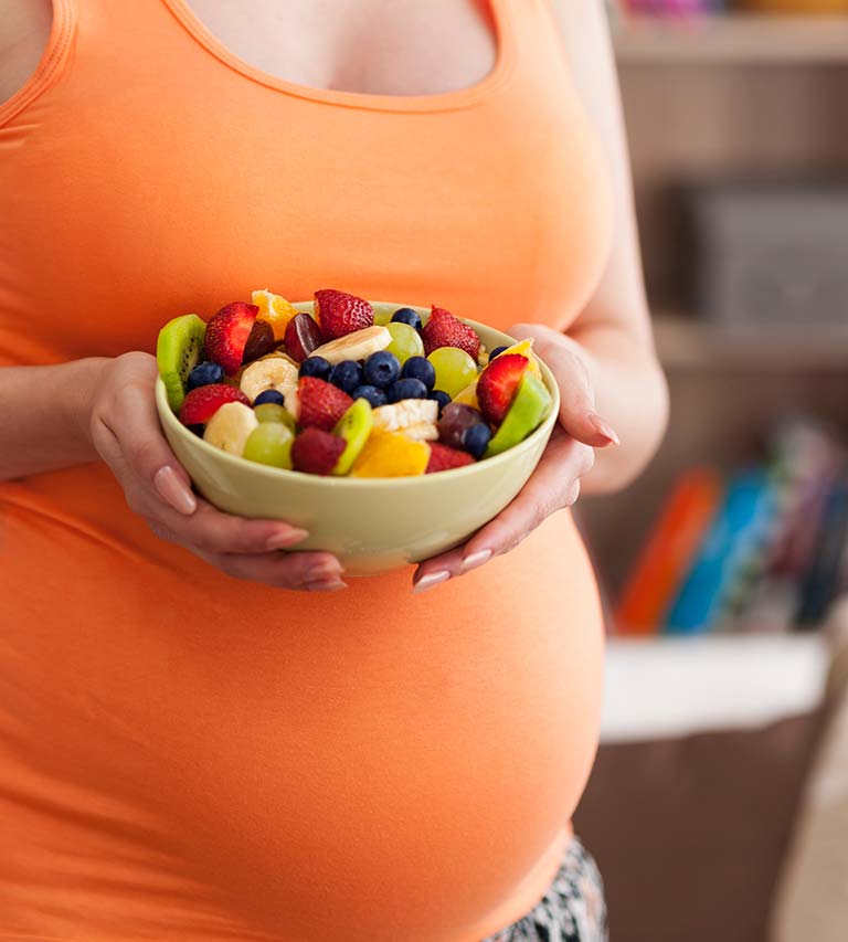 mujer embarazada con plato de fruta con vitaminas prenatales